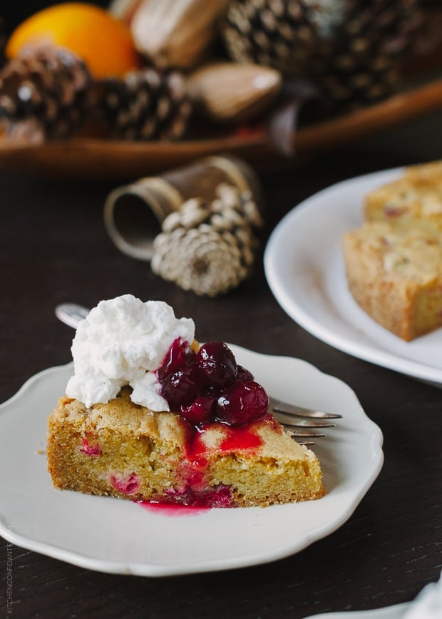 A slice of Cranberry Orange Olive Oil Cake topped with cranberry sauce and whipped cream.