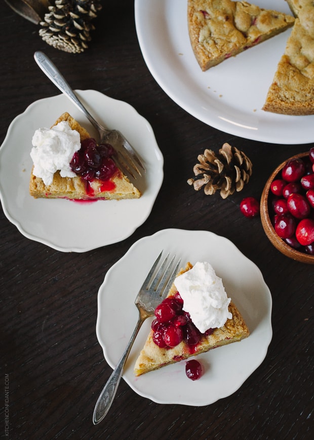 Slices of Cranberry Orange Olive Oil Cake on white plates topped with cranberry sauce and whipped cream.
