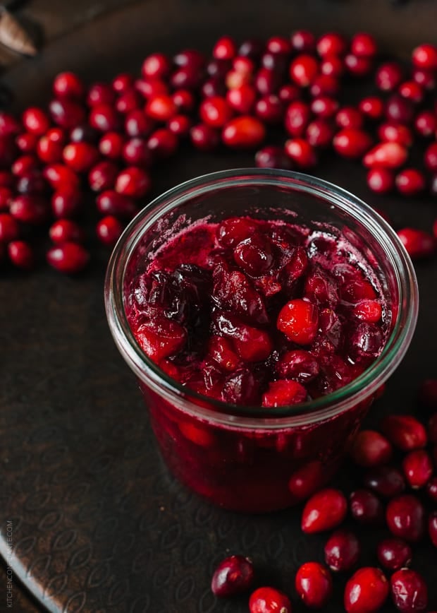 A jar of cranberry sauce surrounded by cranberries.