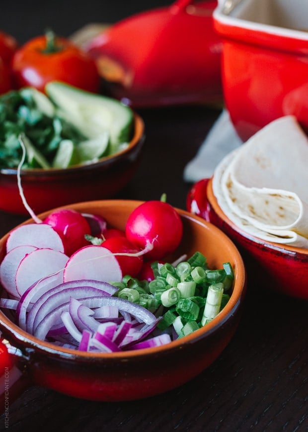 A bowl of toppings for posole including sliced red onions, red onions, and scallions.