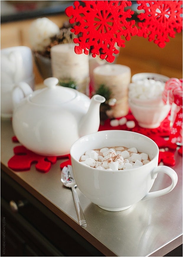 A large mug of hot chocolate and marshmallows, a spoon, and a white teapot.