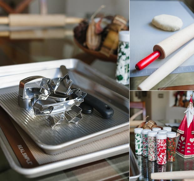 Metal cookie cutters on a cookie sheet, colorful holiday sprinkles, and rolling pins.