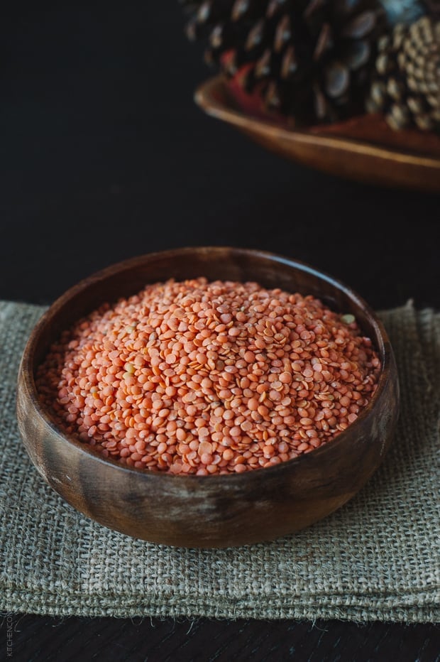 A wooden bowl filled with dried red lentils.