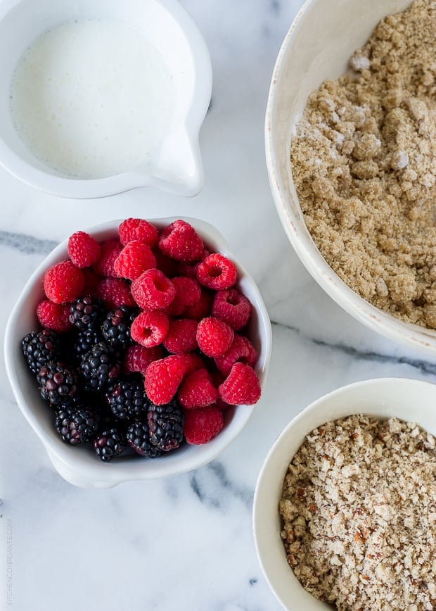 White bowls filled with buttermilk, raspberries, blackberries, and coffee cake ingredients.