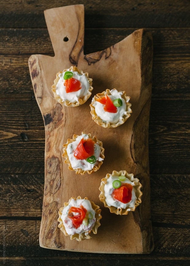 Five smoked salmon appetizers on a wooden serving board.