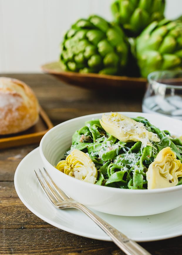 A bowl of green Homemade Spinach Fettuccine with halved artichokes and a creamy chicken sausage sauce. 