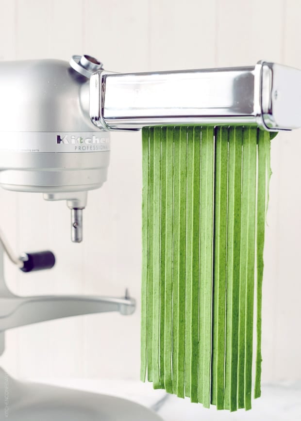 Green spinach fettuccine being extruded from the KitchenAid pasta maker. 