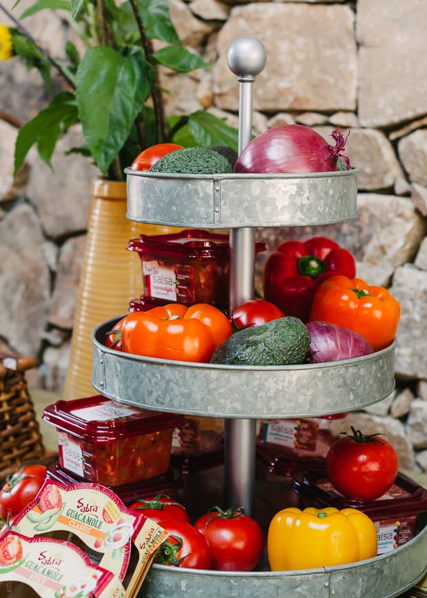 A rustic tiered tower of fresh peppers, tomatoes, and avacadoes.
