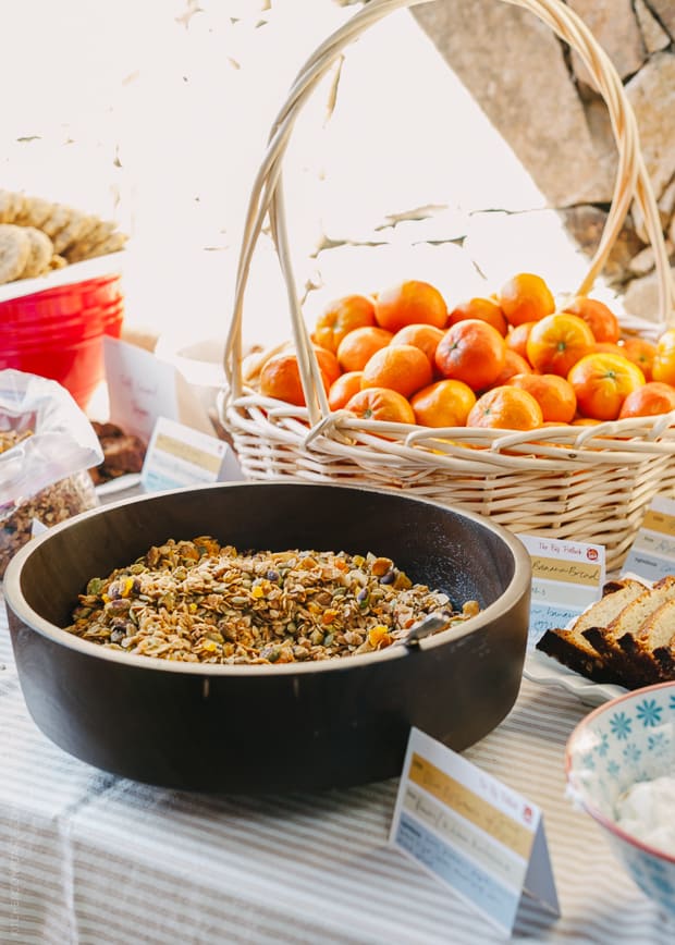 A black serving dish full of granola. A basket of clementines is in the background.