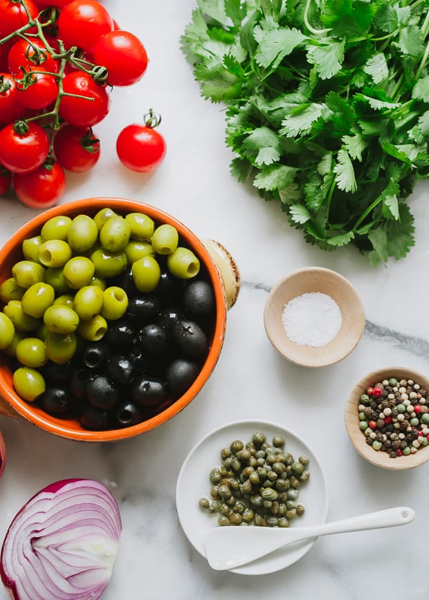 Ingredients used in making Tomato Olive Salsa: olives, cherry tomatoes, cilantro, salt, peppercorns, capers, and onion.