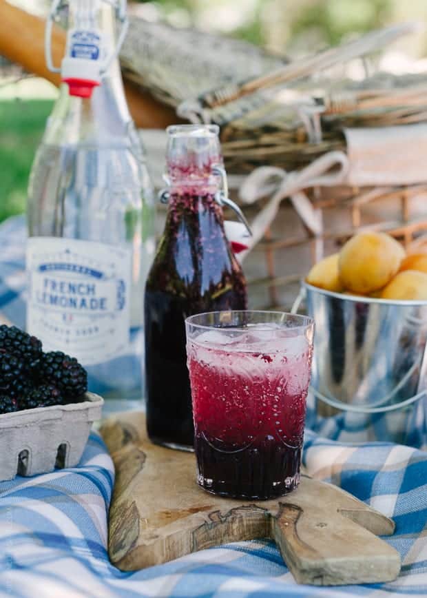 A glass filled with Blackberry Shrub Lemonade at a picnic.