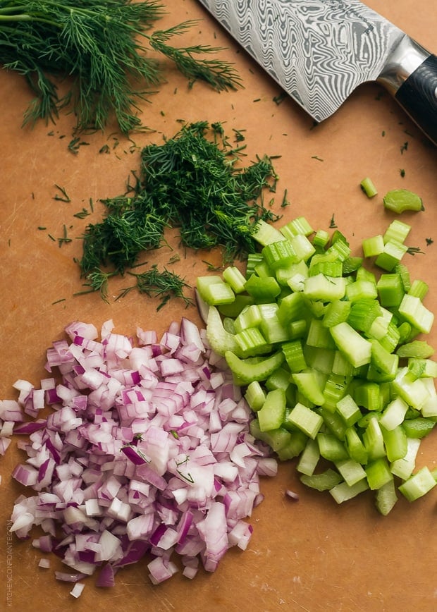 Chopped red onion, dill, and celery on a cutting board.