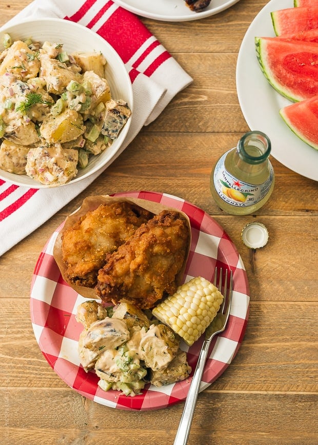 Fried chicken, Buffalo Ranch Grilled Potato Salad, and corn on the cob on a paper plate.