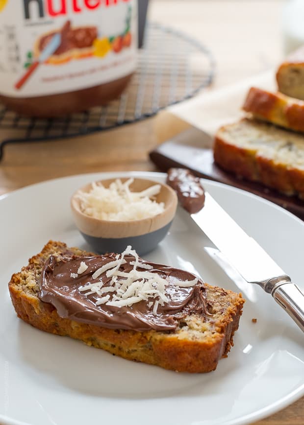 A slice of Coconut Banana Bread on a white plate. The bread is spread with Nutella, then sprinkled with additional coconut.