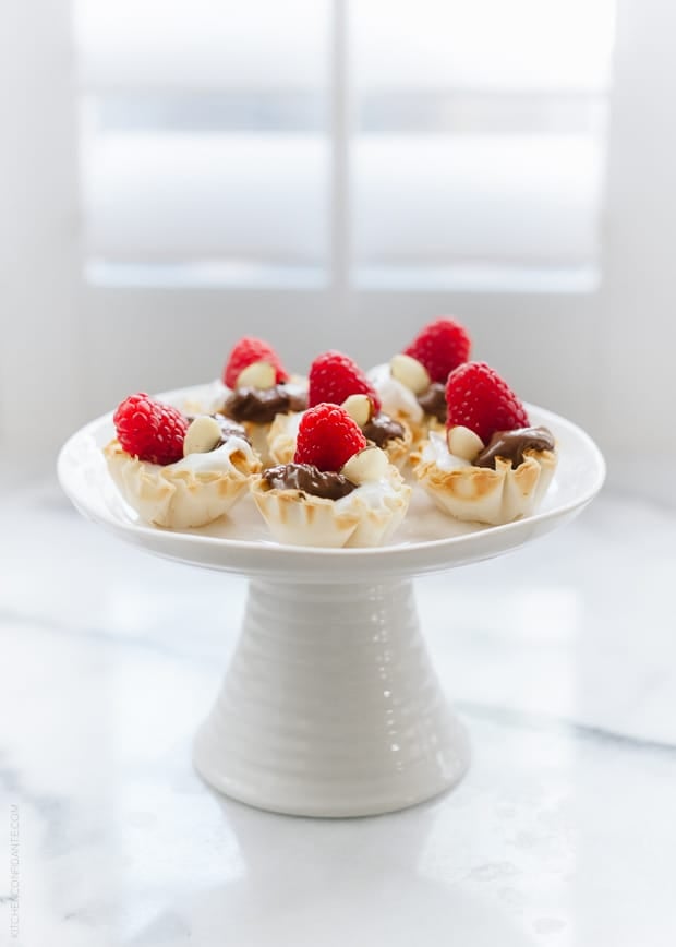 Nutella Greek Yogurt Phyllo Cups topped with fresh raspberries arranged on a white cake stand.