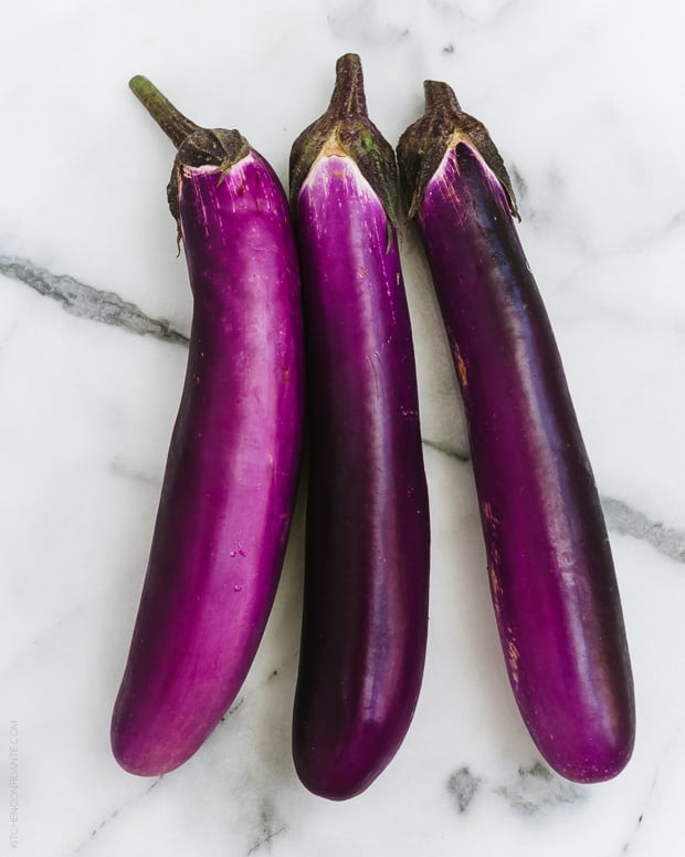 Three Japanese eggplants on a marble surface.