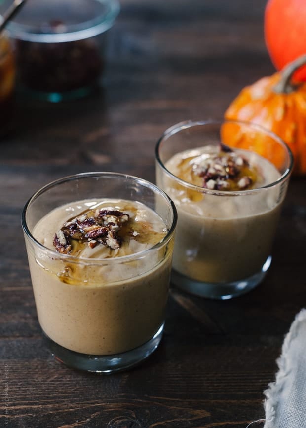 Two glasses filled with Pumpkin Butter Smoothie and topped with a drizzle of honey and candied pecans.