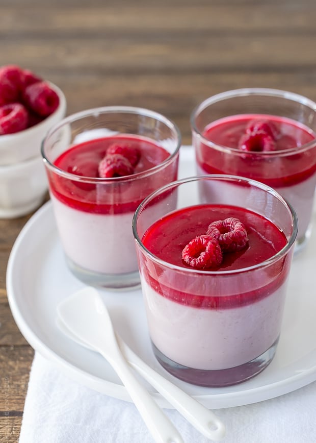 A white plate holding three glass dishes of layered raspberry panna cotta.