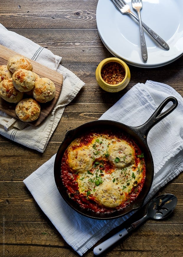 Cast iron skillet filled with baked eggs and biscuits alongside on a wooden surface.