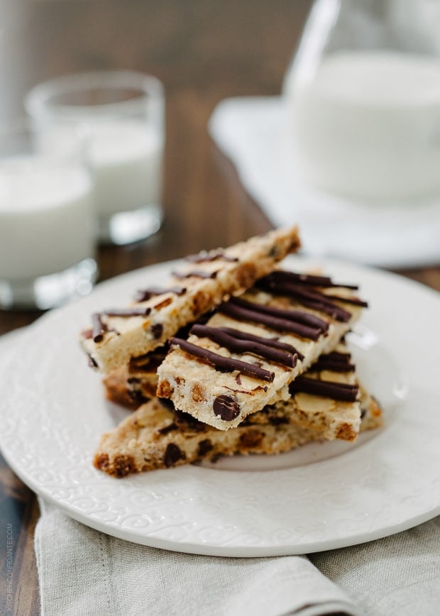 Chocolate Butterscotch Cookie Brittle stacked on a white plate with glasses of milk in the background.