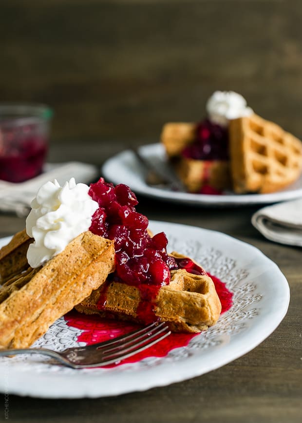 Gingerbread Belgian Waffles served on a white plate with cranberry compote and a whipped cream topping.