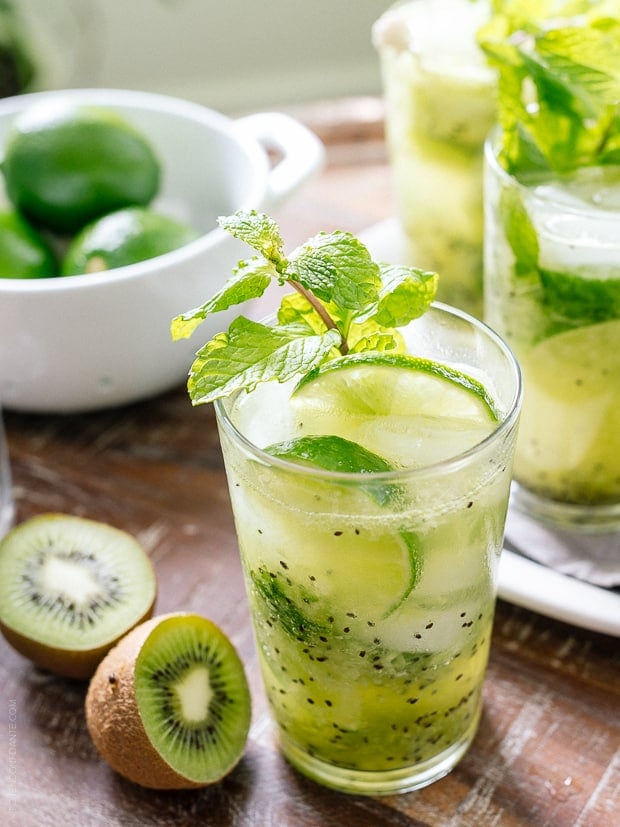 Kiwi Lime Mojitos surrounded by fresh kiwi on a wooden surface.