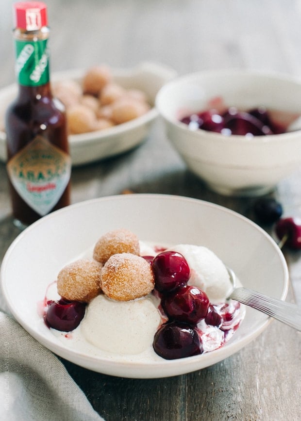 Churro Doughnut Holes with Ice Cream and Cherry Chipotle Sauce in a white bowl.