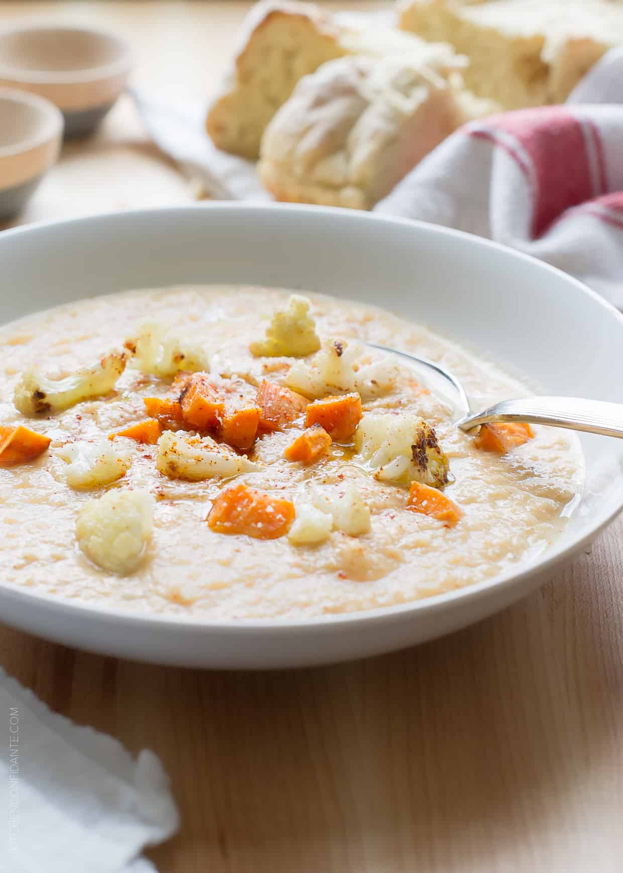 White bowl filled with Roasted Cauliflower and Sweet Potato Chowder and garnished with roasted cauliflower and sweet potatoes. 