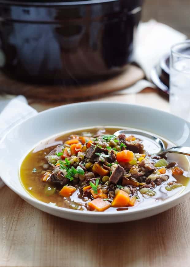 White bowl filled with Prime Rib Beef and Lentil Soup on a wooden surface.