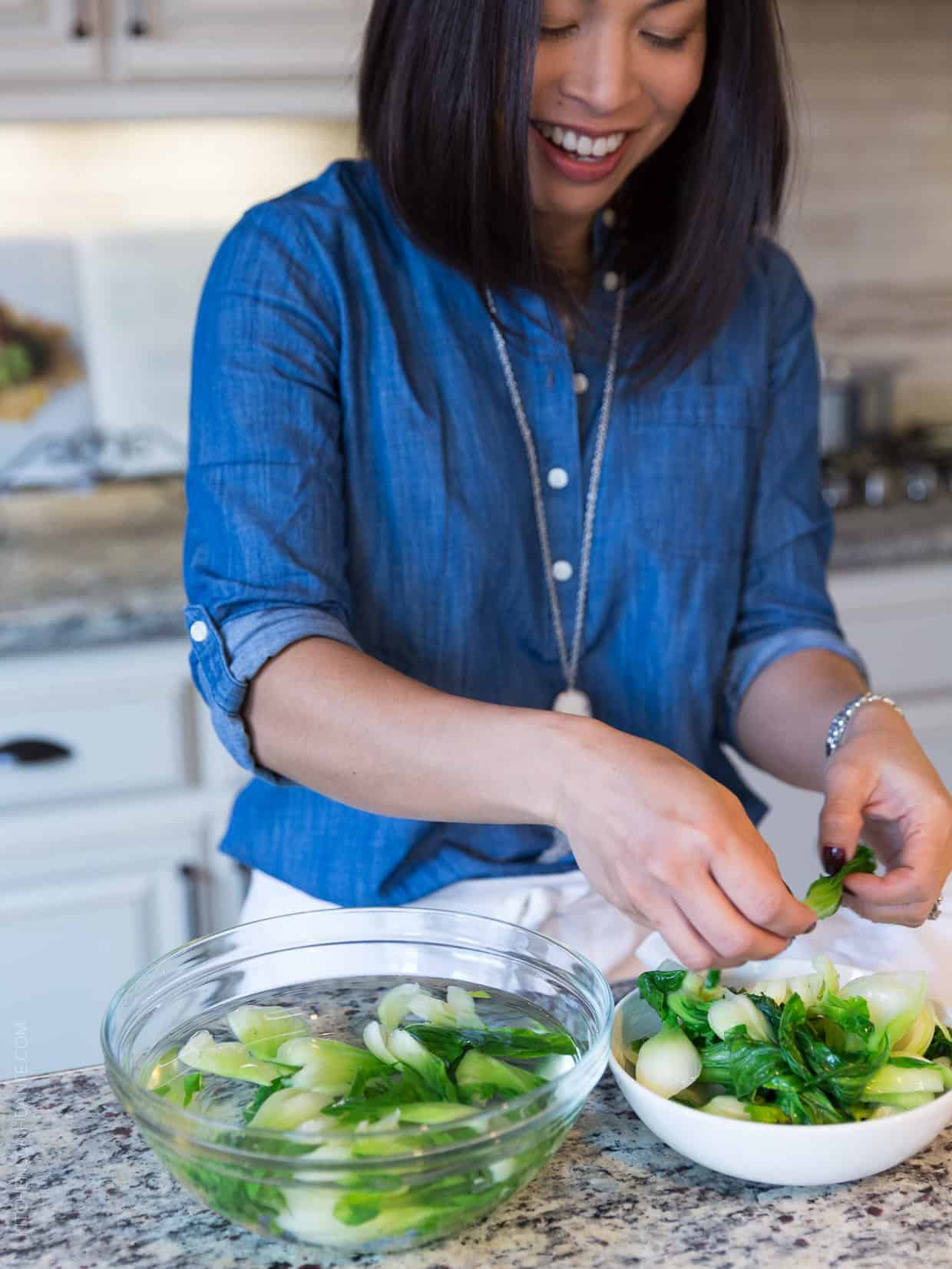 A woman wiht dark hair and a blue shirt preps green vegetables.