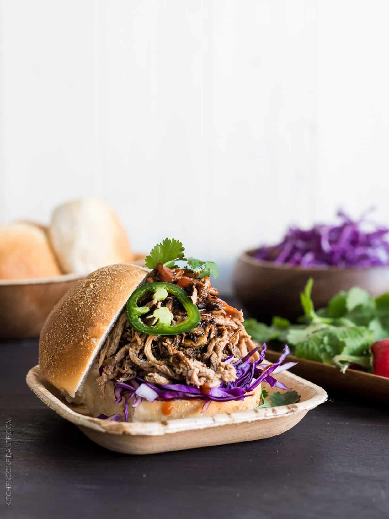 Filipino Adobo-style Pulled Pork Sandwich layered with red cabbage, a few leaves of cilantro and sriracha. 