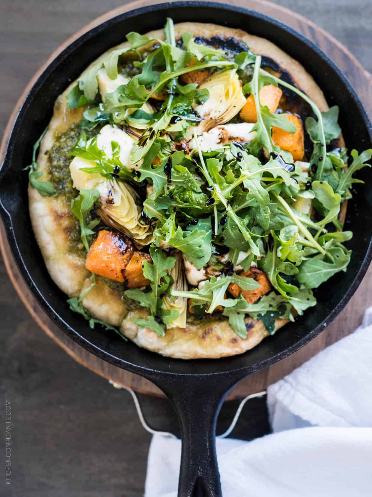 Cast iron skillet filled with Skillet Pesto Flatbread with Goat Cheese, Artichokes and Roasted Butternut Squash.