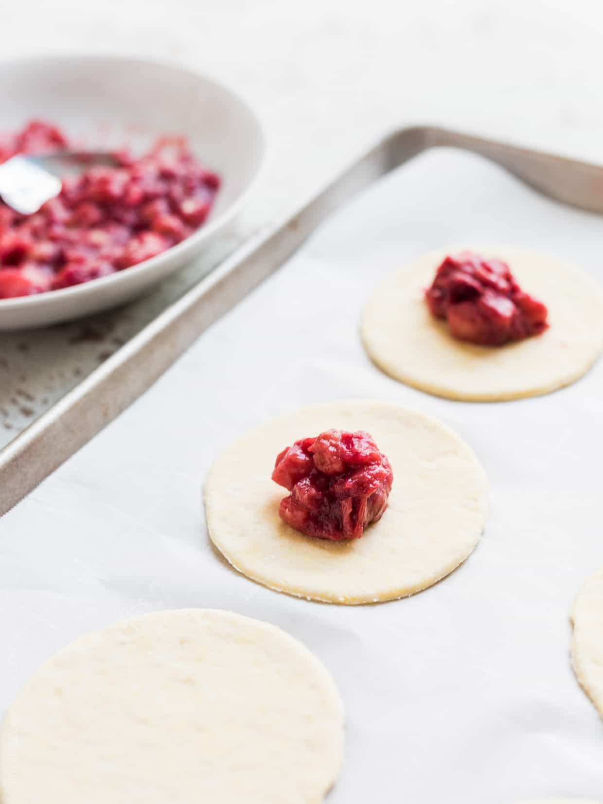 Baking tray with circles of pastry dough topped with rhubarb filling for rhubarb empanadas.