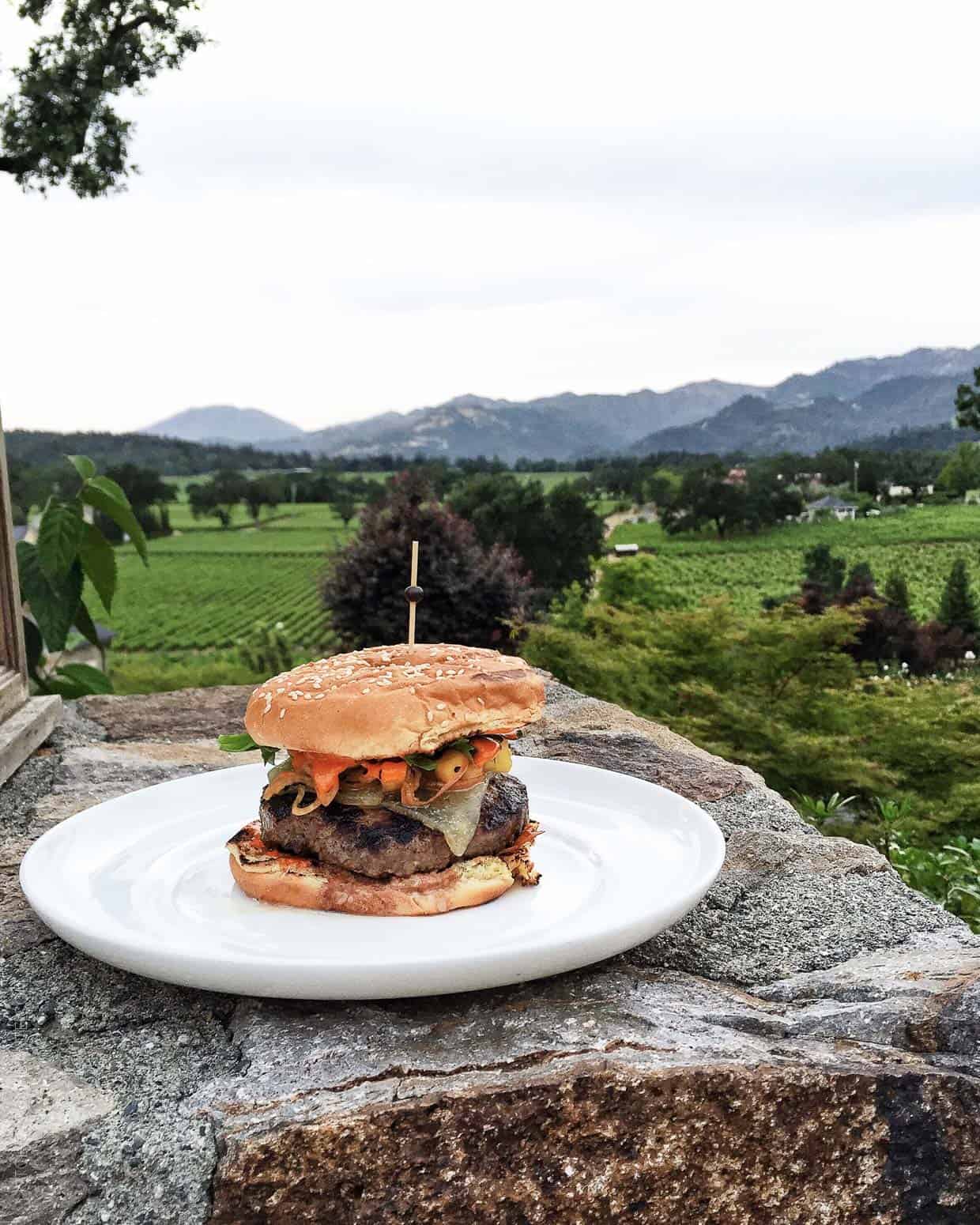 Sweet and Smoky Spanish Beef Burger on a white plate on a rock outdoors.