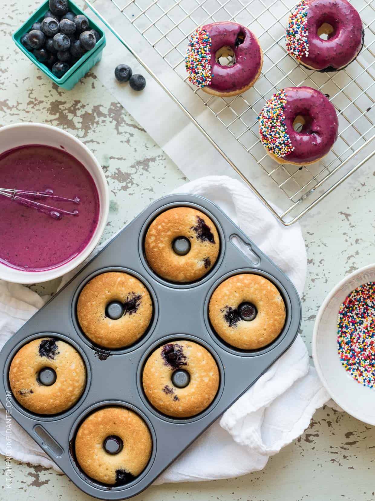 Freshly baked Blueberry Lemon Glazed Baked Donuts about to be glazed and topped with multi-colored sprinkles.
