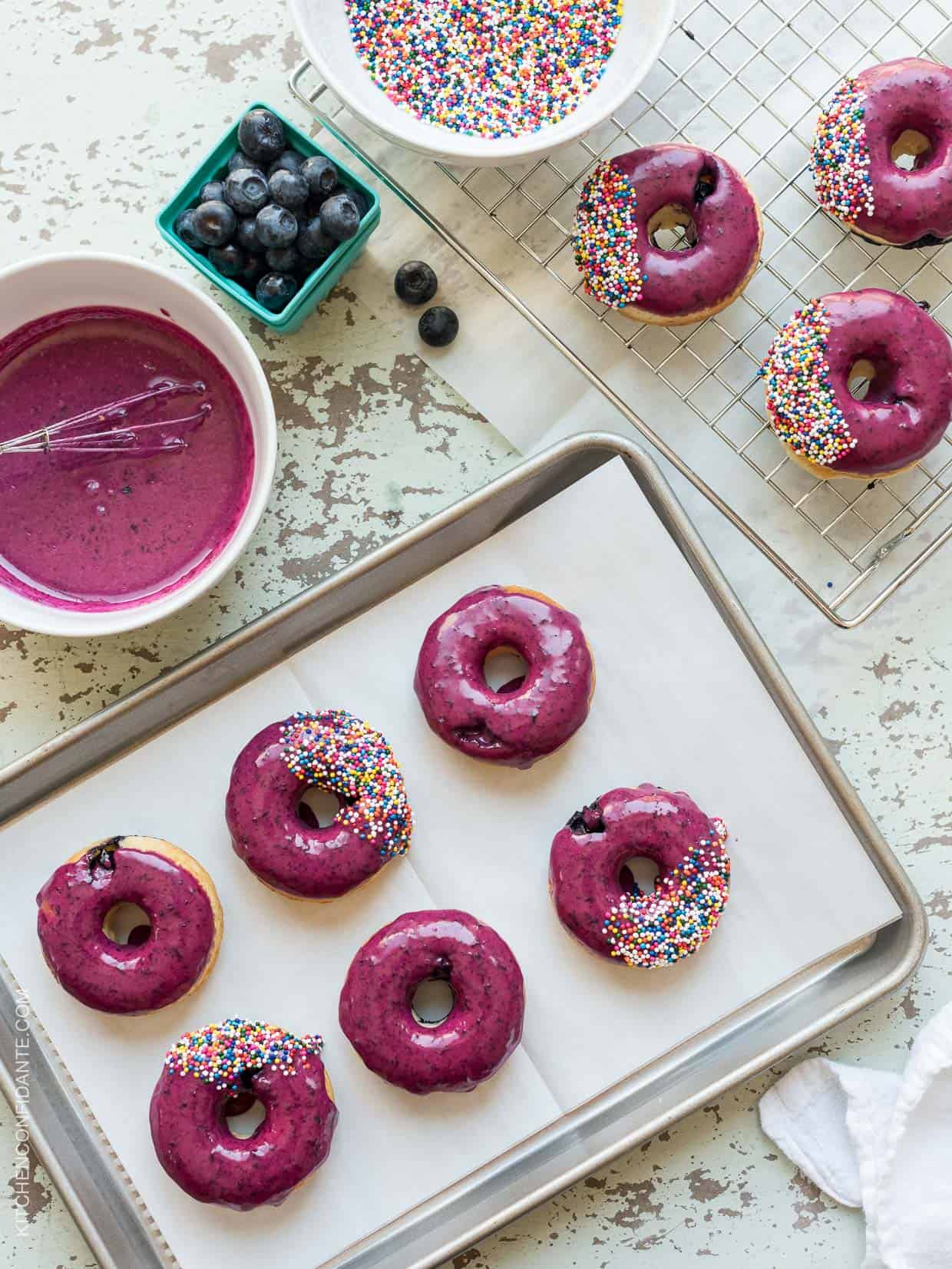 Baking tray of Baked Blueberry Donuts with Blueberry Lemon Glaze and sprinkles on top.