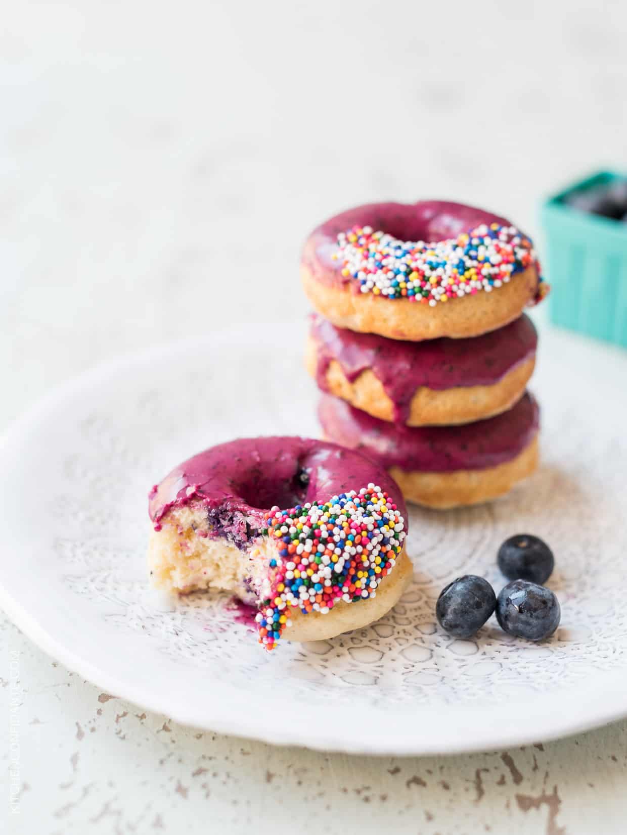 Baked Blueberry Donuts with Blueberry Lemon Glaze on a plate, one with a bite taken out of it.