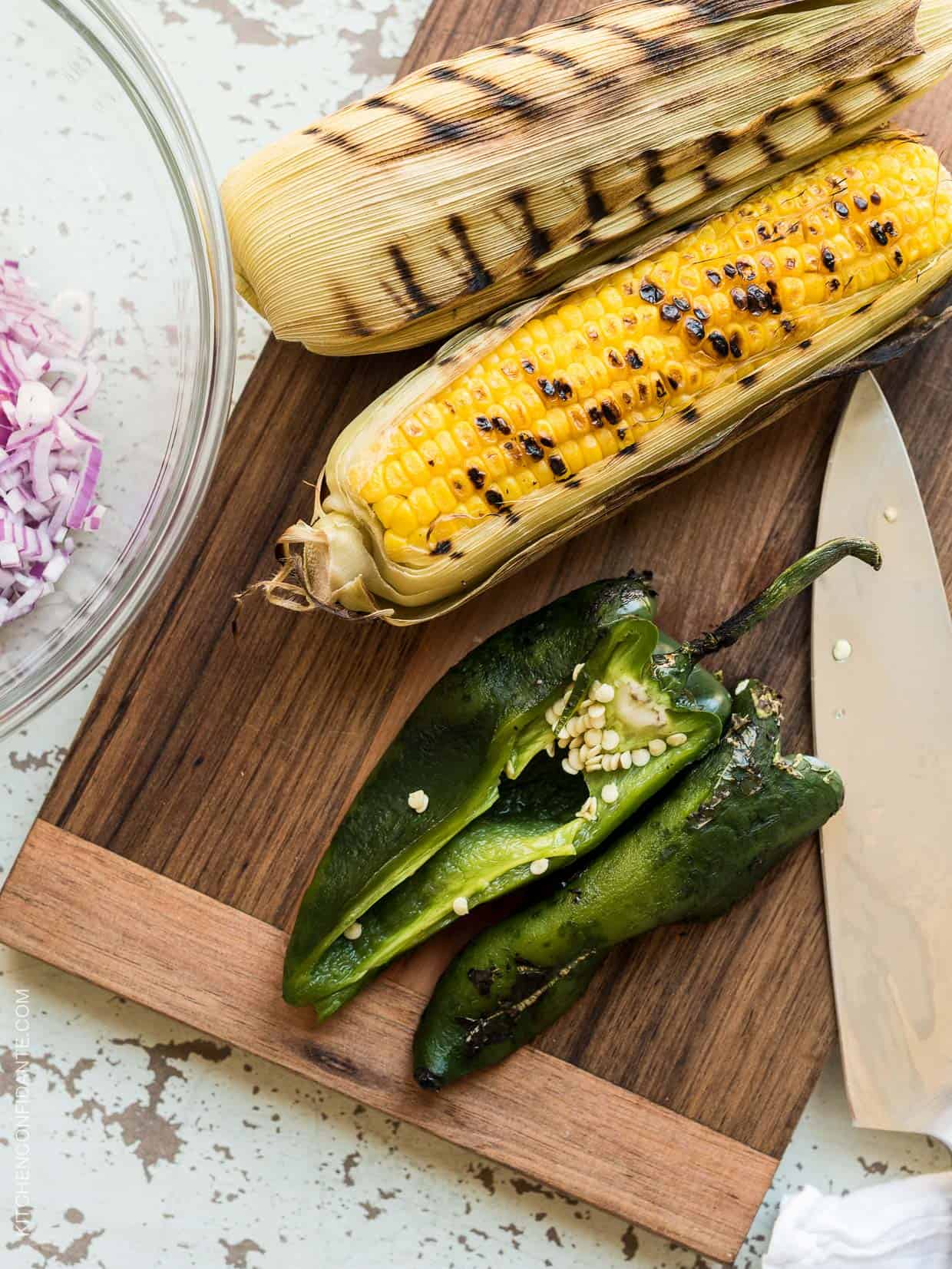 Freshly grilled corn and poblano pepper on a wooden cutting board.