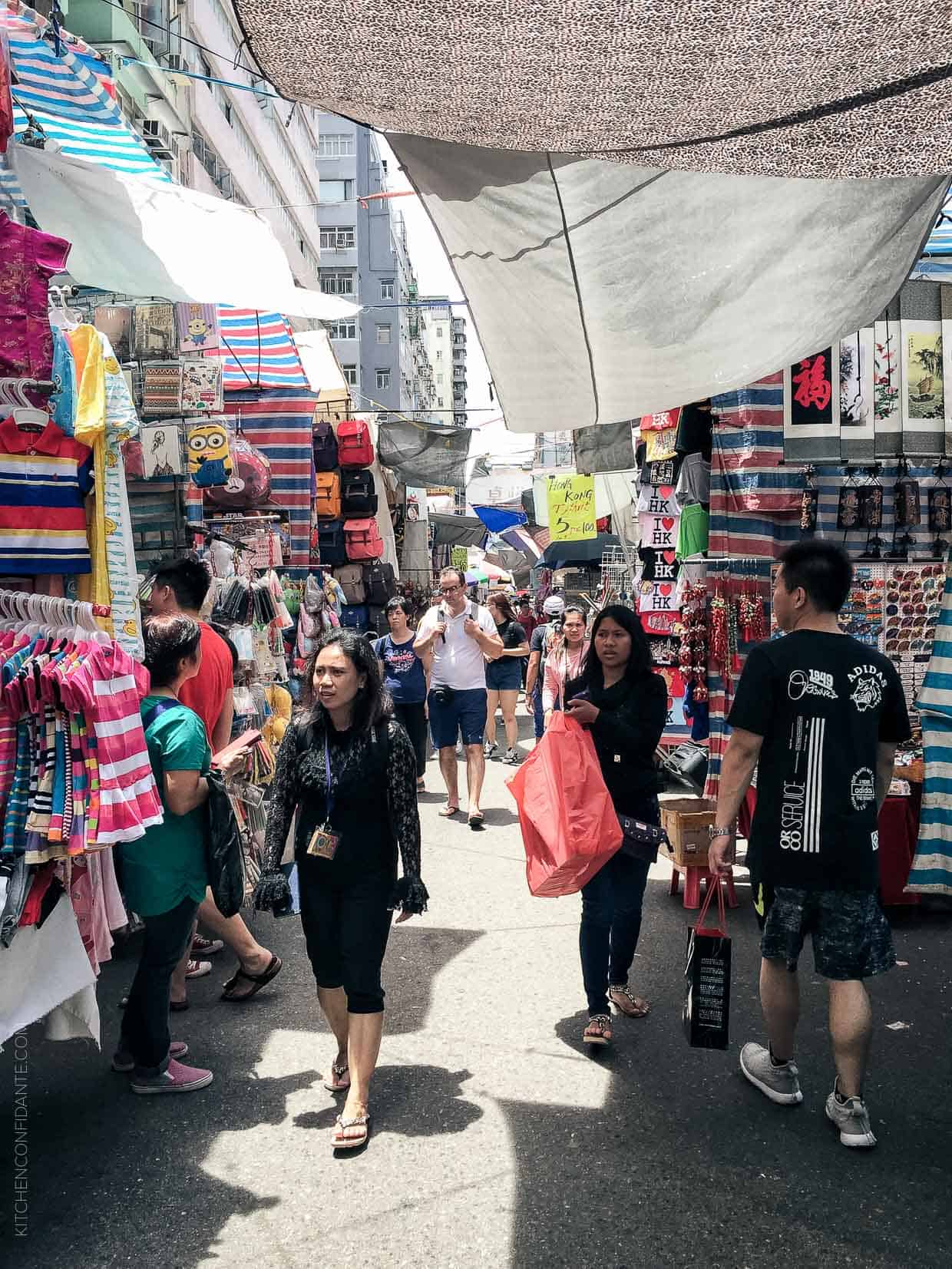 Tightly packed shops on a market street selling clothes, backpacks, and tourist souveniers.