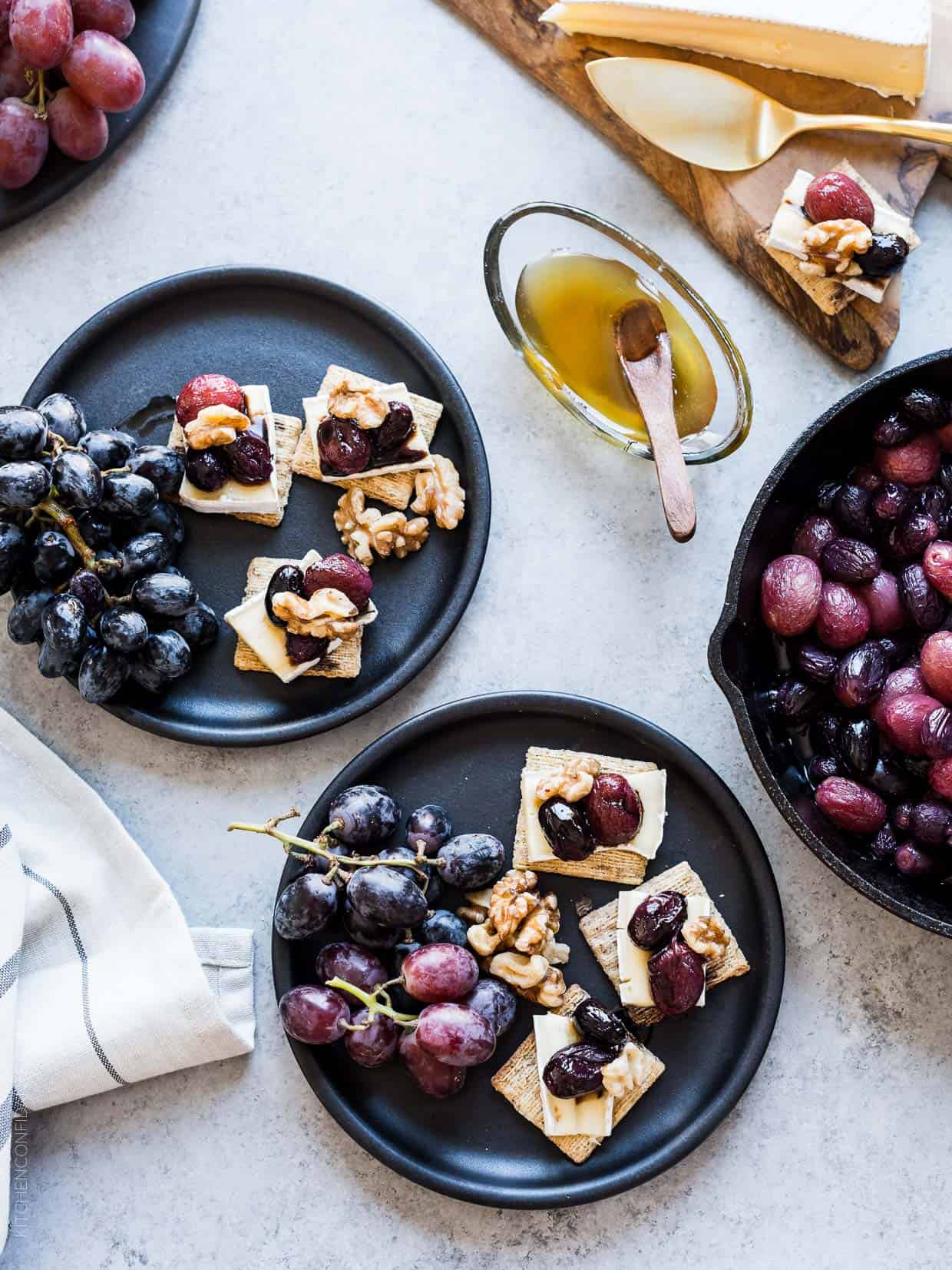 Caramelized Grape, Brie and Walnut Bites made with TRISCUIT crackers and served on dark plates with bunches of grapes.