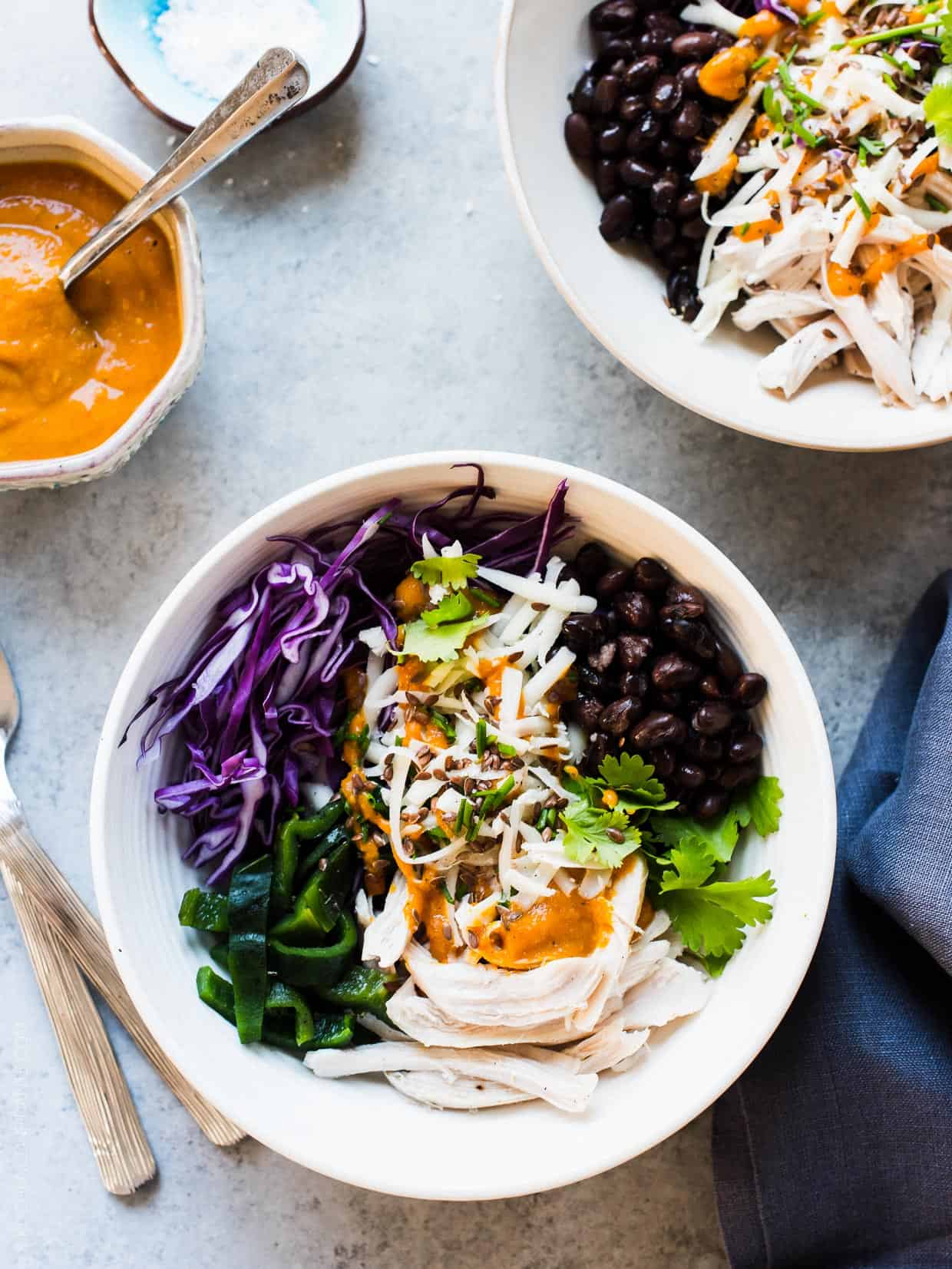 A fresh salad prepared with shredded chicken, cabbage, black beans, charred poblanos, and pumpkin-red curry vinaigrette served in a white bowl.