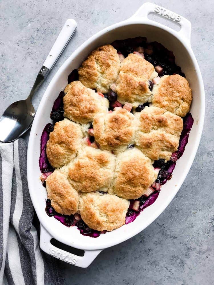 Blueberry Rhubarb Cobbler in a white oval baking dish on a grey surface.