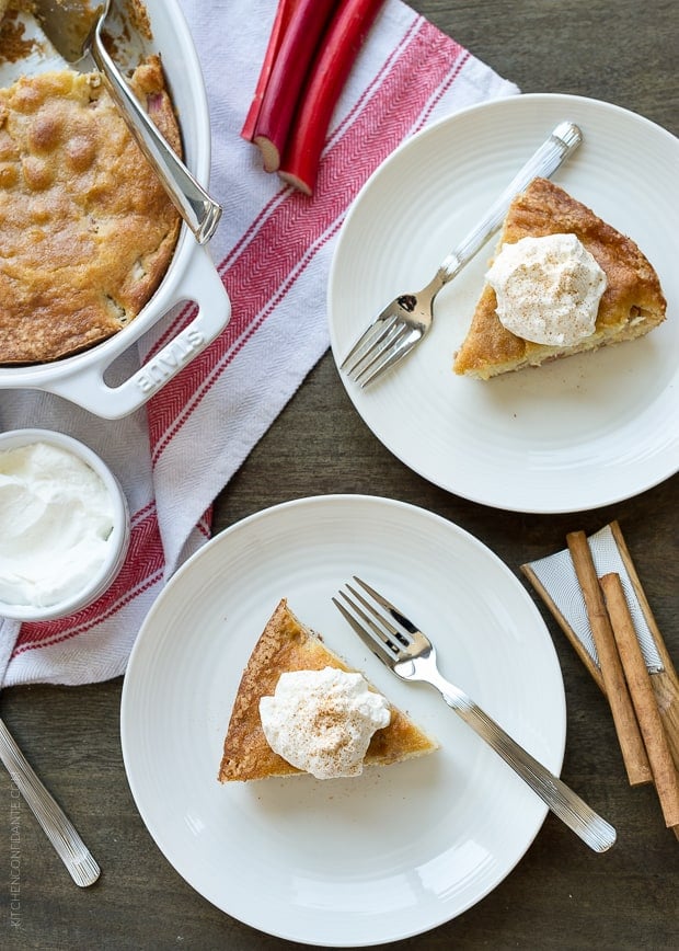 Slices of rhubarb cake topped with spoonfuls of whipped cream on white plates.