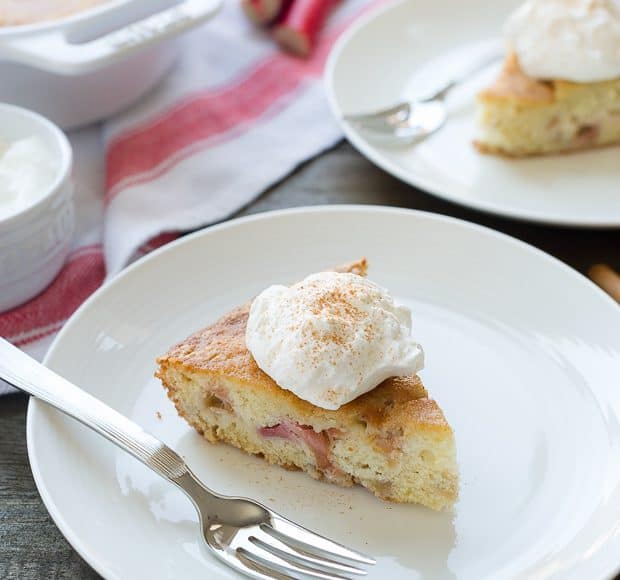 A slice of rhubarb cake topped with whipped cream on a white plate.