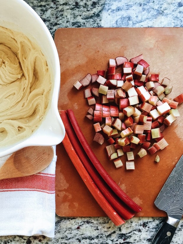 Chopped rhubarb on a cutting board alongside a batter bowl filled with cake batter.