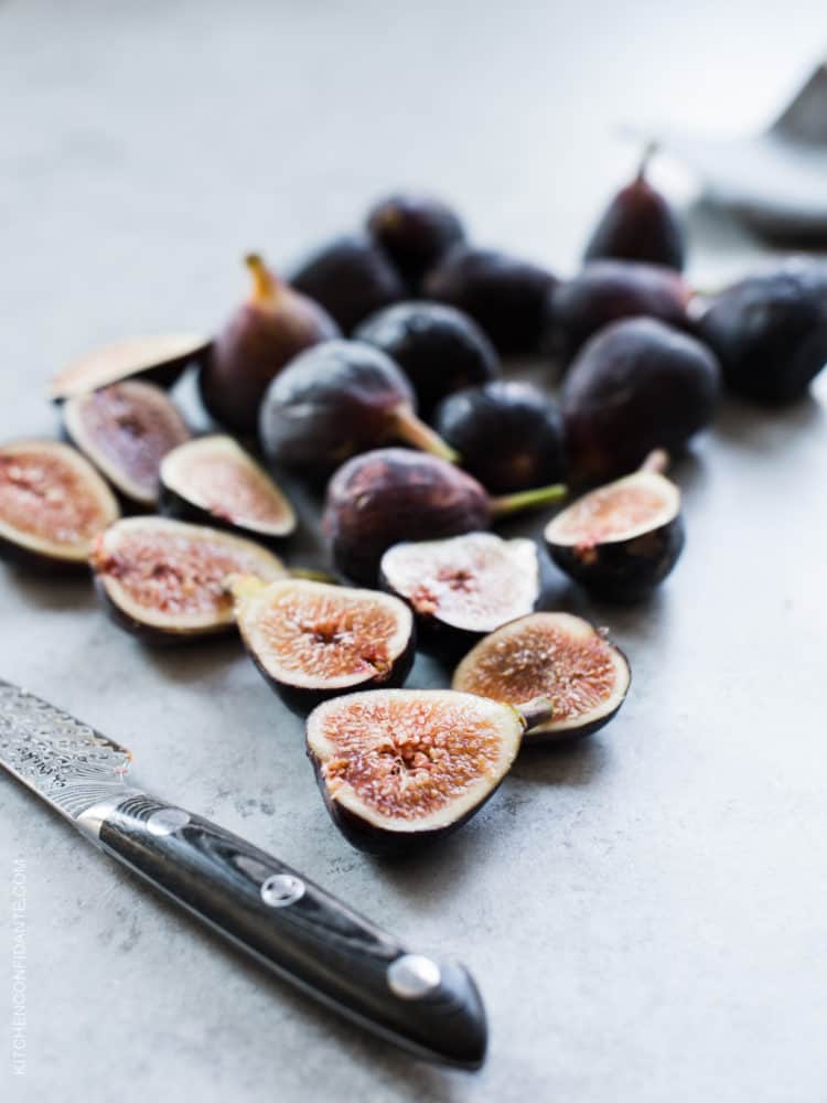 Figs on a cutting board, with most still whole, and several cut in half.