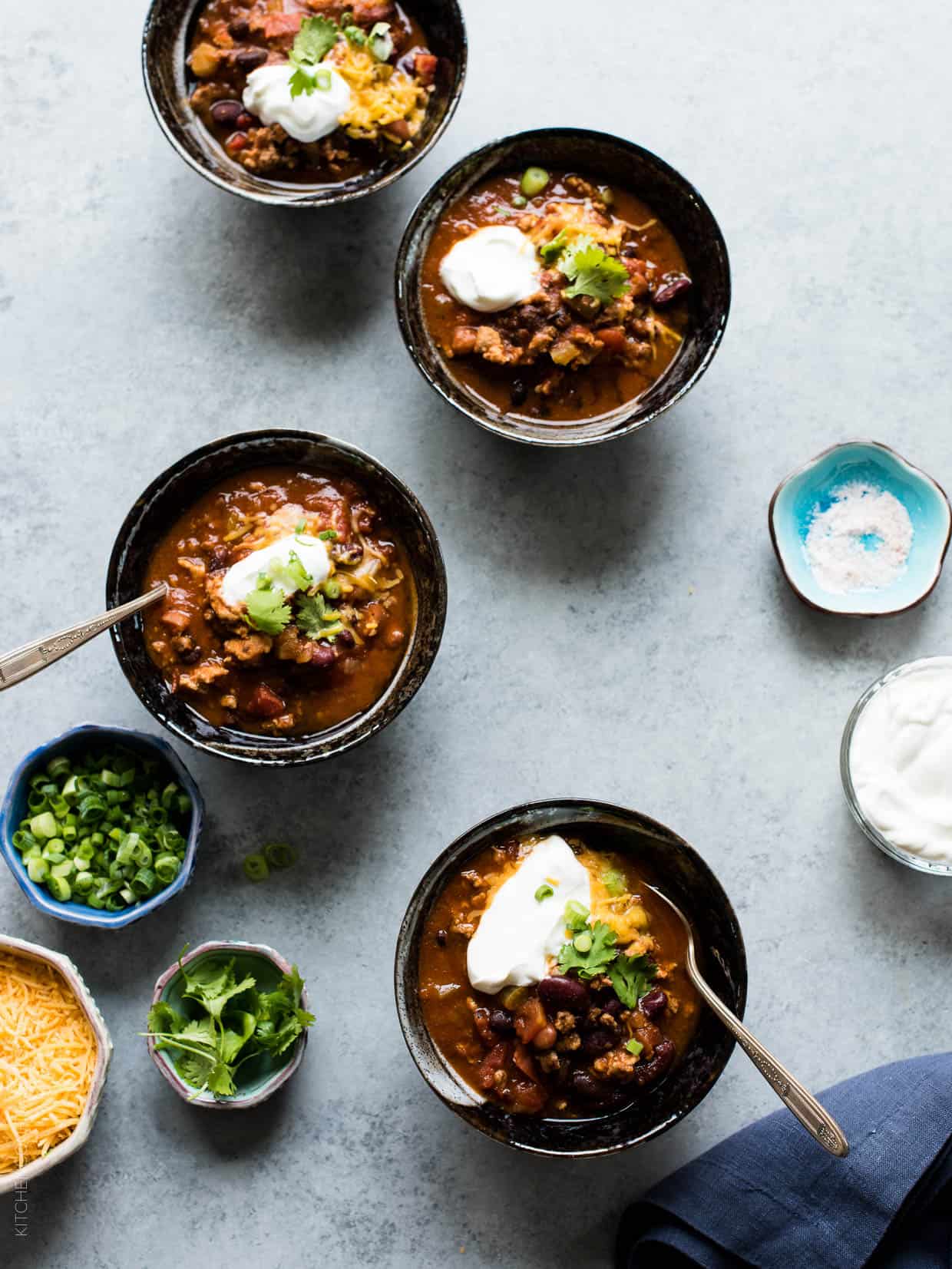 Four bowls of Classic Chili garnished with shredded cheese, sour cream, green onions and cilantro. 