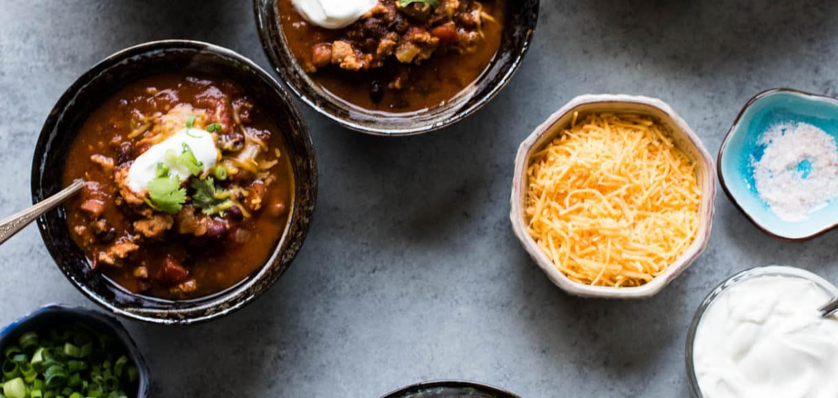 Four bowls of Classic Chili garnished with shredded cheese, sour cream, green onions and cilantro.