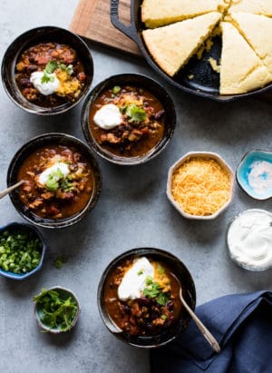 Four bowls of Classic Chili garnished with shredded cheese, sour cream, green onions and cilantro.