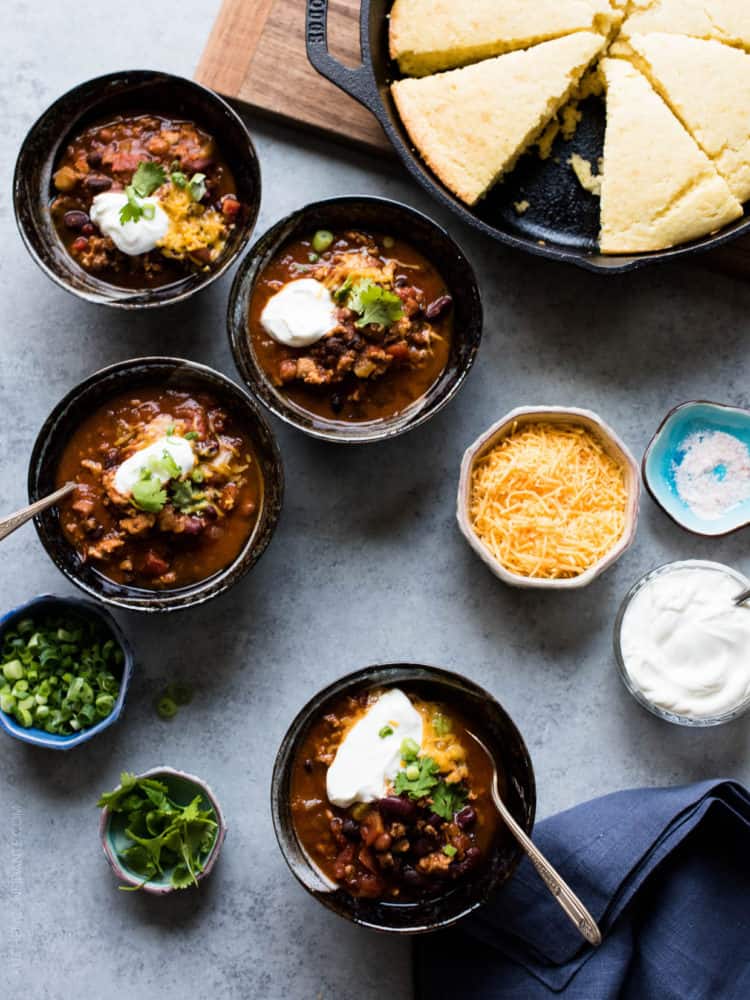 Four bowls of Classic Chili garnished with shredded cheese, sour cream, green onions and cilantro.